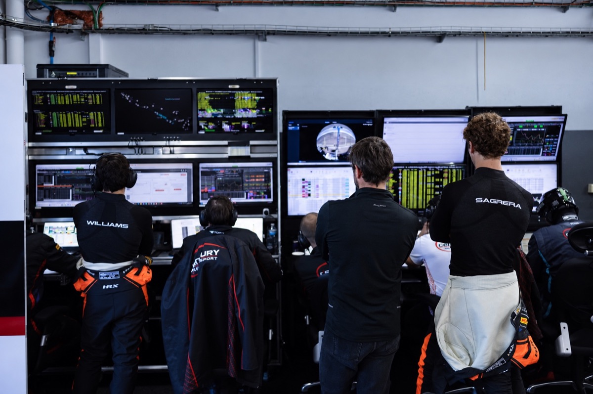 Drivers and engineers reviewing live telemetry at a pit-garage workstation