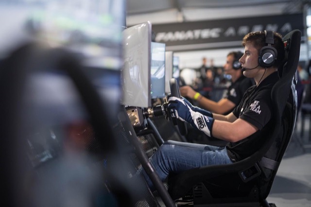 A racing driver using a professional simulator with a steering wheel, display and headset