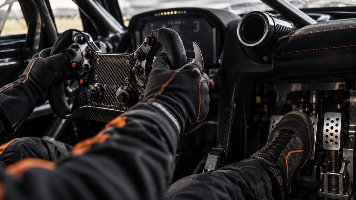 A racing driver applying precise steering and pedal inputs inside a GT cockpit